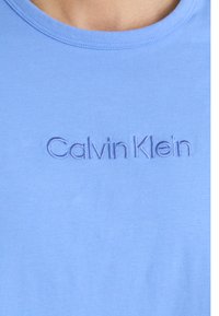 Svetlo modré bavlnené tričko s okrúhlym výstrihom a vyvýšenou výšivkou textu "Calvin Klein" umiestnenou na hrudi.