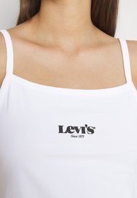Vit linne med tunna axelband, med en svart Levi's-logotyp och texten "Sedan 1873". Slät textur, enkel design.