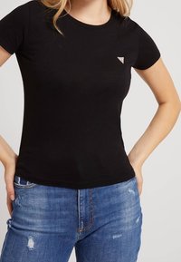 Sort tætsiddende T-shirt lavet af blød bomuld, med rund hals og korte ærmer. Lille trekantet logodetalje på venstre bryst.