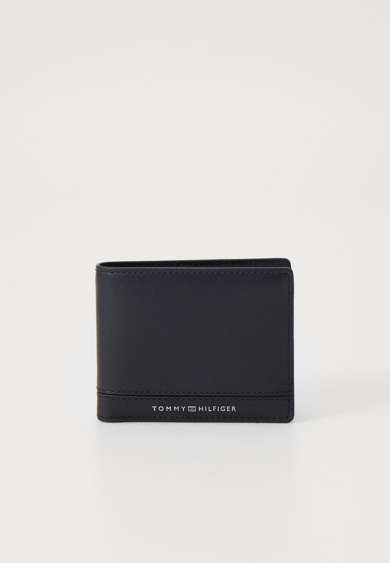 Czarny skórzany portfel o gładkiej powierzchni, w formacie bi-fold, z subtelnym przeszyciem. Na przedniej stronie znajduje się logo "TOMMY HILFIGER" w kolorze srebrnym.