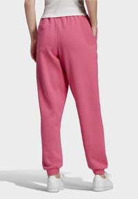 Pantalons de jogging roses avec une taille élastique et des chevilles resserrées, dotés d'une poche arrière et d'une texture douce, associés à des baskets blanches.