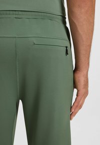 Green athletic trousers feature a fitted design with a zippered pocket on the back, smooth texture, and elastic waistband for comfort.