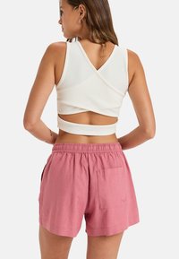 Biele rebrované crop top s prekríženým chrbtom; kombinované s farebnými ľanovými šortkami v ružovej farbe s elastickým pásom a zadnou vreckom.