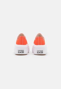 Chaussures en toile orange vif à enfiler avec une semelle en caoutchouc blanche et des surpiqûres contrastées, arborant le logo "CONVERSE ALL STAR" sur le talon.