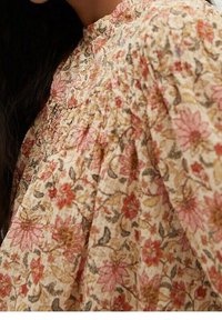 Blumenbluse aus leichtem Stoff mit beigem Hintergrund und rosa- und braunfarbenen Blumenmustern, geraffte Details am Ausschnitt.