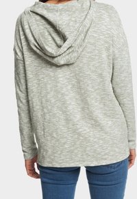 Sweat à capuche gris clair avec une texture douce et une finition texturée, équipé d'une capuche à cordon de serrage et d'une coupe décontractée, porté avec un jean bleu.