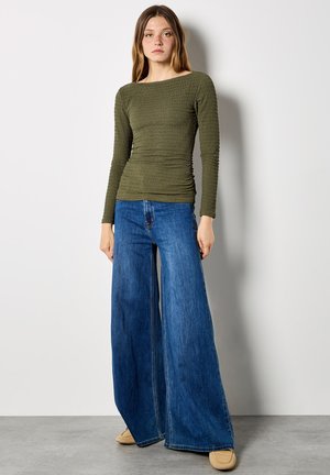 Olive green, long-sleeve, fitted top with textured, ruched fabric paired with high-waisted, wide-leg, light blue jeans. Smooth, soft shoes.