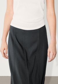 Jupe gris foncé en tissu tissé, présentant des coutures avant et une finition lisse, associée à un haut blanc ajusté.