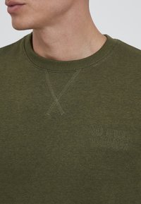 Olívazöld pulóver kerek nyakkivágással, textúrált keresztszemes részlettel és egy finom "BLEND DENIM" logóval a mellrészen.