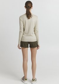 Beige langermet topp med en tettsittende design, kombinert med mørkegrønne shorts. Antrekket har en jevn tekstur og en avslappet stil.