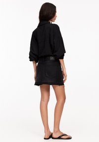 Chemise noire surdimensionnée avec épaules basses, associée à une mini-jupe en denim noir avec un ourlet effiloché et des détails de couture minimalistes. Sandales noires.