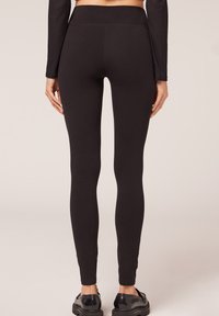 Schwarze Leggings mit einem hohen Bund, aus einem glatten, dehnbaren Material, figurbetont an den Beinen, ohne sichtbare Muster oder Hardware.
