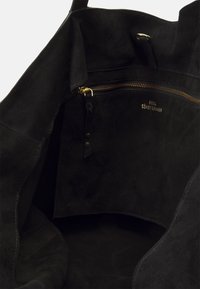 Black suede tote bag interior, featuring a gold zipper pocket, smooth texture, and a subtle embossed logo detail.