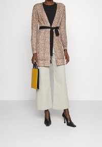 Kardigan w panterkę z czarnym paskiem, noszony na czarnym topie, w połączeniu z jasnobeżowymi szerokimi spodniami i czarnymi szpilkami, trzymający żółtą torebkę.