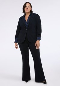 Námořnický texturovaný oblek s dobře padnoucím sakem a rozšířenými kalhotami, se zářezovým límcem a zapínáním na jeden knoflík, doplněný tmavě modrou blůzou.