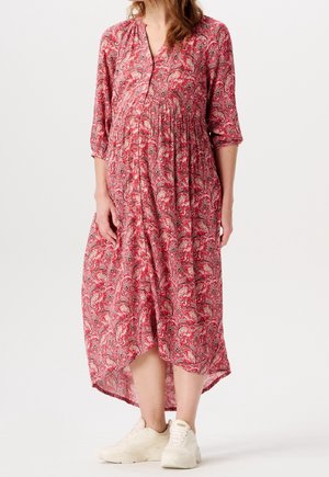 Rode maxi-jurk met paisleyprint, driekwartmouwen, V-hals en een geplooide taille, gecombineerd met witte sneakers. De zoom is langer aan de achterkant.