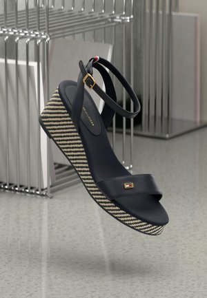 Granatowy sandał na koturnie z paskiem na kostkę, platformą z tkaniny w paski oraz złotymi ozdobami. Gładka faktura i otwarty przód.