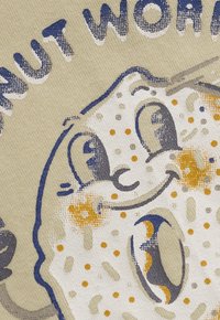 Uśmiechający się kartonowy gąbka z dużymi oczami i pomarańczowymi plamkami, otoczony częściowo widocznym tekstem na beżowym tle z materiału.