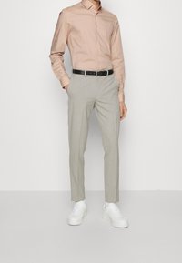 Světle růžová košile, béžové tailored kalhoty a bílé tenisky. Černý opasek dotváří outfit, který má přiléhavý siluetu a hladké textury.