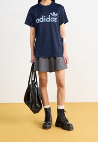 Marinblå Adidas-t-shirt med ljusblå logotyp, kombinerad med en grå plisserad kjol. Svarta läderkängor och en svart väska fulländar outfiten.