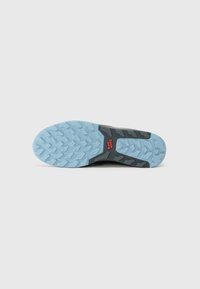 Semelle de chaussure de sport au design robuste ; partie supérieure gris-noir, semelle extérieure bleu clair texturée, motifs de grip proéminents et détail de logo rouge.