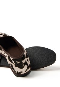 Scarpe slip-on con stampa bovina, upper in morbido tessuto, dettagli marroni e suola in gomma nera testurizzata per grip e durata.