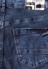 Jeans en denim bleu marine dotés d'une poche arrière avec un design de couture distinct et d'une étiquette positionnée sur la ceinture.