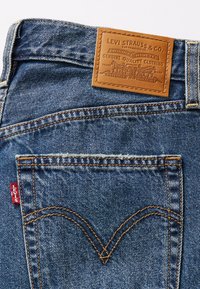 Blauwe denim jeans met een bruine leren patch met reliëfbranding. Zichtbare stiksels en een rode Levi's logo-label op de achterzak.