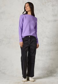 Lila Strickpullover mit rundem Halsausschnitt, kombiniert mit schwarzen Cordhosen und weißen Turnschuhen. Sanfte Textur, lockere Passform.