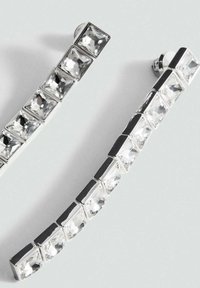 Orecchini in tonalità argento con più cristalli trasparenti a taglio quadrato disposti in un design lineare con una leggera curvatura. Accenti in metallo lucido.