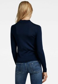 Marineblauer Langarmpullover mit geripptem Kragen, tailliertem Schnitt und glatter Textur, kombiniert mit hellblauen, verwaschenen Jeans.
