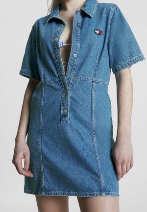 Sukienka jeansowa w jasnoniebieskim kolorze, z krótkimi rękawami, zapięciem na guziki z przodu oraz naszywką z logo na piersi. Posiada dopasowaną talię i prosty dół.