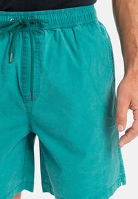 Teal simbyxor gjorda av lättviktsmaterial med elastisk midja, snörning och sidofickor. Sval känsla och avslappnad passform.