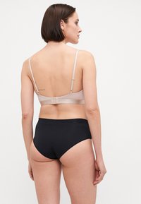 Lyserød bh med justerbare stropper og hægtslukning, parret med sorte højtaljede trusser, glat stof, minimalistisk design.