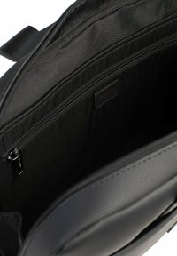 Interno della borsa per laptop nera con rivestimento in tessuto, dotata di un ampio scomparto e una tasca con zip, texture morbida, design minimalista.