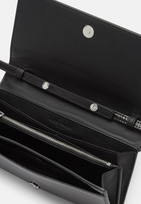 Czarny skórzany portfel o gładkiej fakturze. Posiada zapięcie na zatrzask, kieszeń na zamek błyskawiczny i wytłoczone logo. Wnętrze ma wiele slotów na karty.