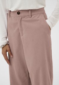 Ružičaste kordor pants s opuštenim krojem, s kopčanjem na dugme, bočnim džepovima i mekim materijalom. Uparene s bijelom košuljom s dugim rukavima.