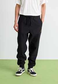 Pantaloni sport negri, cu talie ajustabilă prin șnur, având un detaliu subtil cu logo. Fabricat dintr-un material neted, cu croială conică și manșete elastice.
