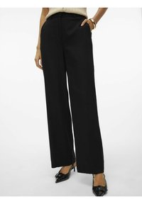 Pantalons larges noirs avec une texture lisse, dotés de poches latérales, d'une taille haute et d'une coupe ajustée, complétés par des talons aigus noirs.