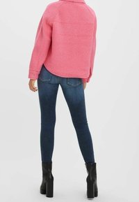 Lyserød tekstureret jakke med krave, parret med mørkeblå skinny jeans og sorte platformstøvler. Taget bagfra mod en hvid baggrund.