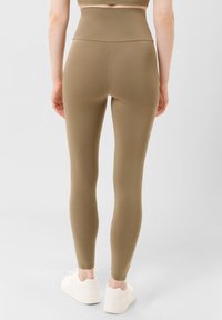 Vysoké legíny v khaki zelené barvě, vyrobené z hladkého, pružného materiálu. Mají přiléhavý střih, který se zužuje k kotníkům. Nosí se s bílými teniskami.