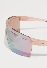 Nike Course sunčane naočale s prozirnim okvirom u ružičastoj boji, gradijentnim lećama u plavoj i ljubičastoj boji te plavim logotipom na sljepoočnici.