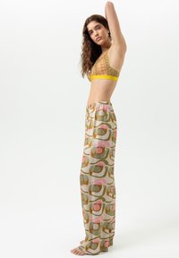 Gehäkelter Bustier in Olivgrün mit gelber Kante, kombiniert mit weit geschnittenen Hosen mit retro-inspirierten pastellfarbenen geometrischen Mustern auf hellem Hintergrund.