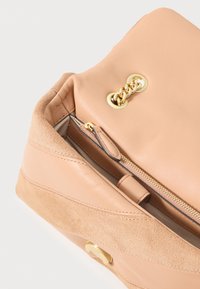 Bolsa de couro e camurça em tom bege claro, com um detalhe em corrente dourada, apresentando um bolso com fecho e uma textura suave.