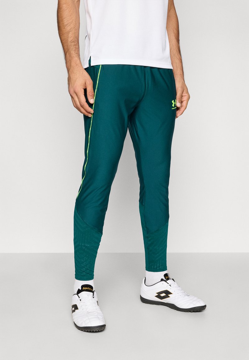 Τιρκουάζ αθλητικό παντελόνι με πράσινες λωρίδες στο πλάι, με στενή εφαρμογή, λεπτομέρεια υφής στο κατώτερο μέρος των ποδιών και αεριζόμενο ύφασμα, σε συνδυασμό με λευκά αθλητικά παπούτσια.