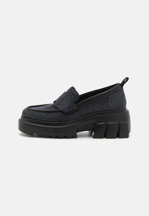 Schwarze Slipper mit einer strukturierten Oberseite, ausgestattet mit einer mittelhohen, klobigen Gummisohle und einem dekorativen Riemen über dem Spann.