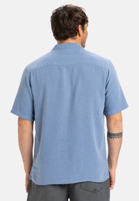 Košeľa s krátkym rukávom, svetlomodrá, s golierom, štruktúrovaná látka a rovný lem. Obsahuje zadný diel a voľný strih.