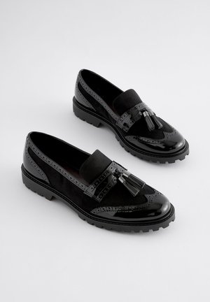Schwarze Loafers aus einer Kombination von glänzendem Lackleder und Wildleder. Mit Quasten, Brogue-Details und einer klobigen Sohle.