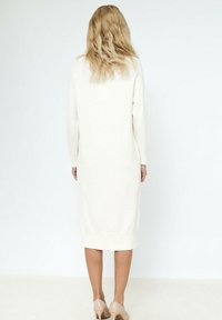 Robe en tricot longue de couleur crème, à manches longues et avec des poignets côtelés, dotée d'une coupe droite et atteignant la mi-mollet.