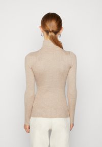 Beigenvärinen ryppylankainen pooloneule, jossa pitkät hihat, kapea istuvuus, pehmeä pinta, korkea kaulus ja keskipitkä selkäosa.